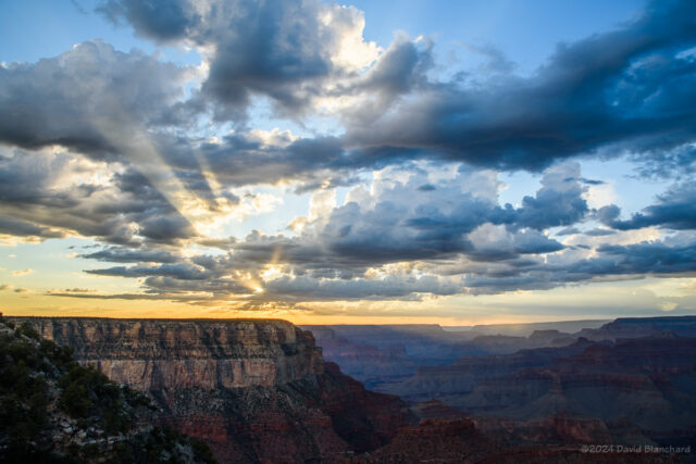 A wider-angle view shows crepuscular rays both in the canyon and the clouds above.